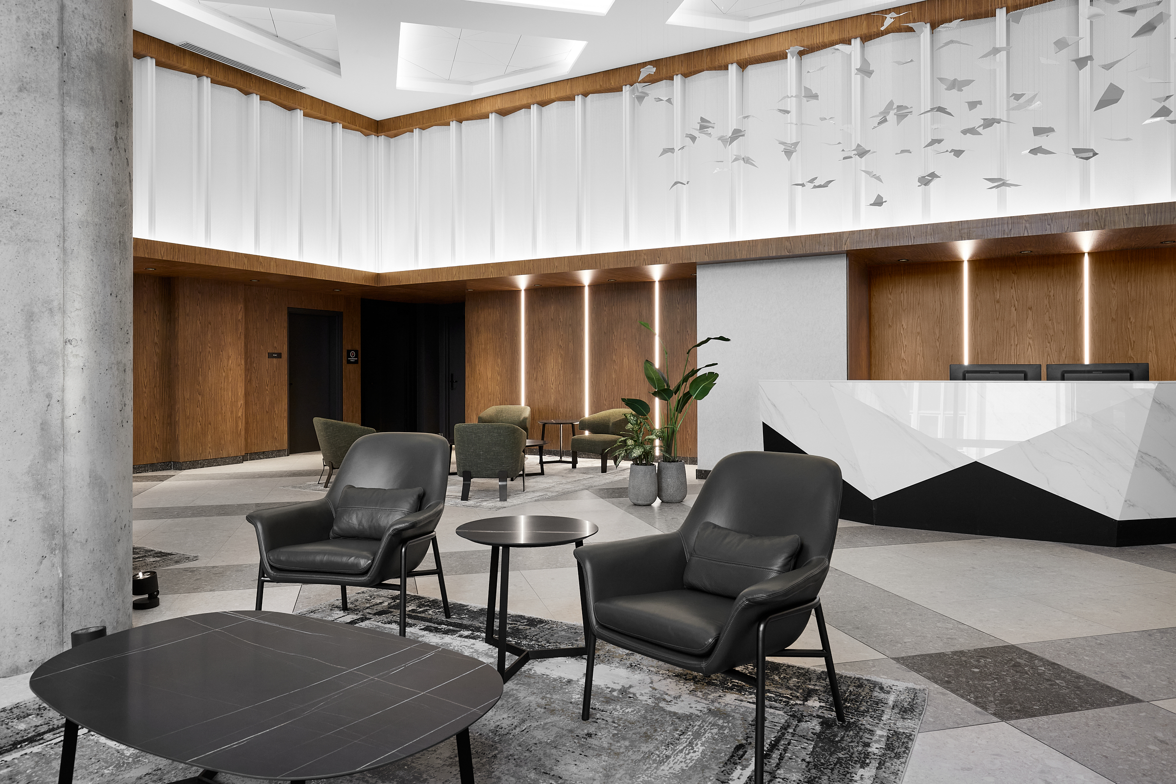 Espace d'accueil moderne avec fauteuils noirs, comptoir de réception et installation de plafond suspendu